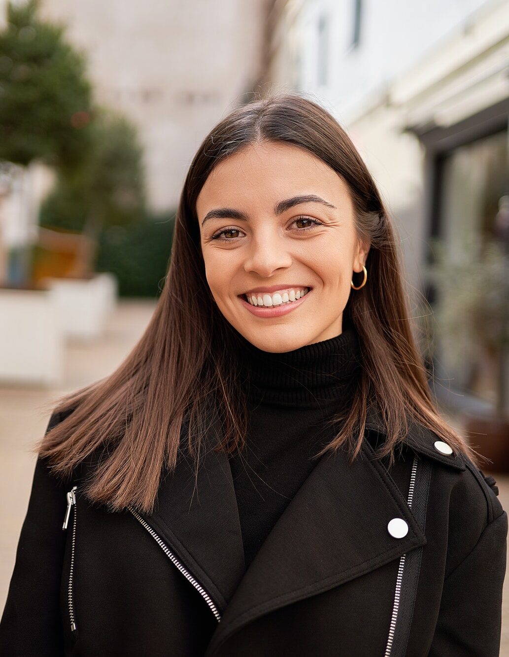 Close-up of a stylish woman smiling while standing outdoors.